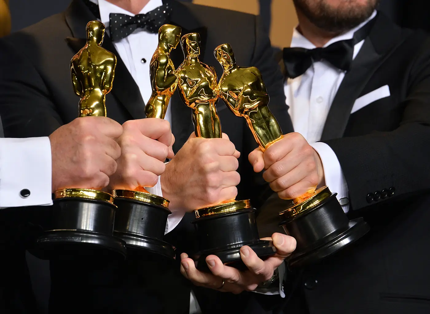 shutterstock_675634309 - VIPshow Čtyři muži v tmavých oblecích v rukách drží zlatou filmovou sošku