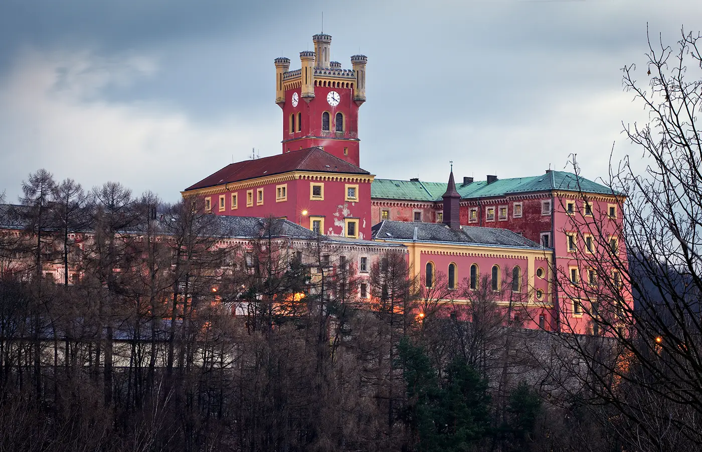 Červený hrad za šera obklopený stromy s opadanými listy