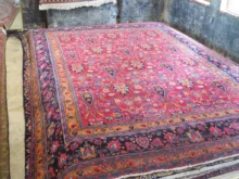 Large colorful Persian-style rug with a red field and ornate floral border laid over a workshop floor.