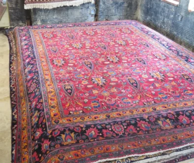 Large colorful Persian-style rug with a red field and ornate floral border laid over a workshop floor.