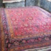 Large colorful Persian-style rug with a red field and ornate floral border laid over a workshop floor.