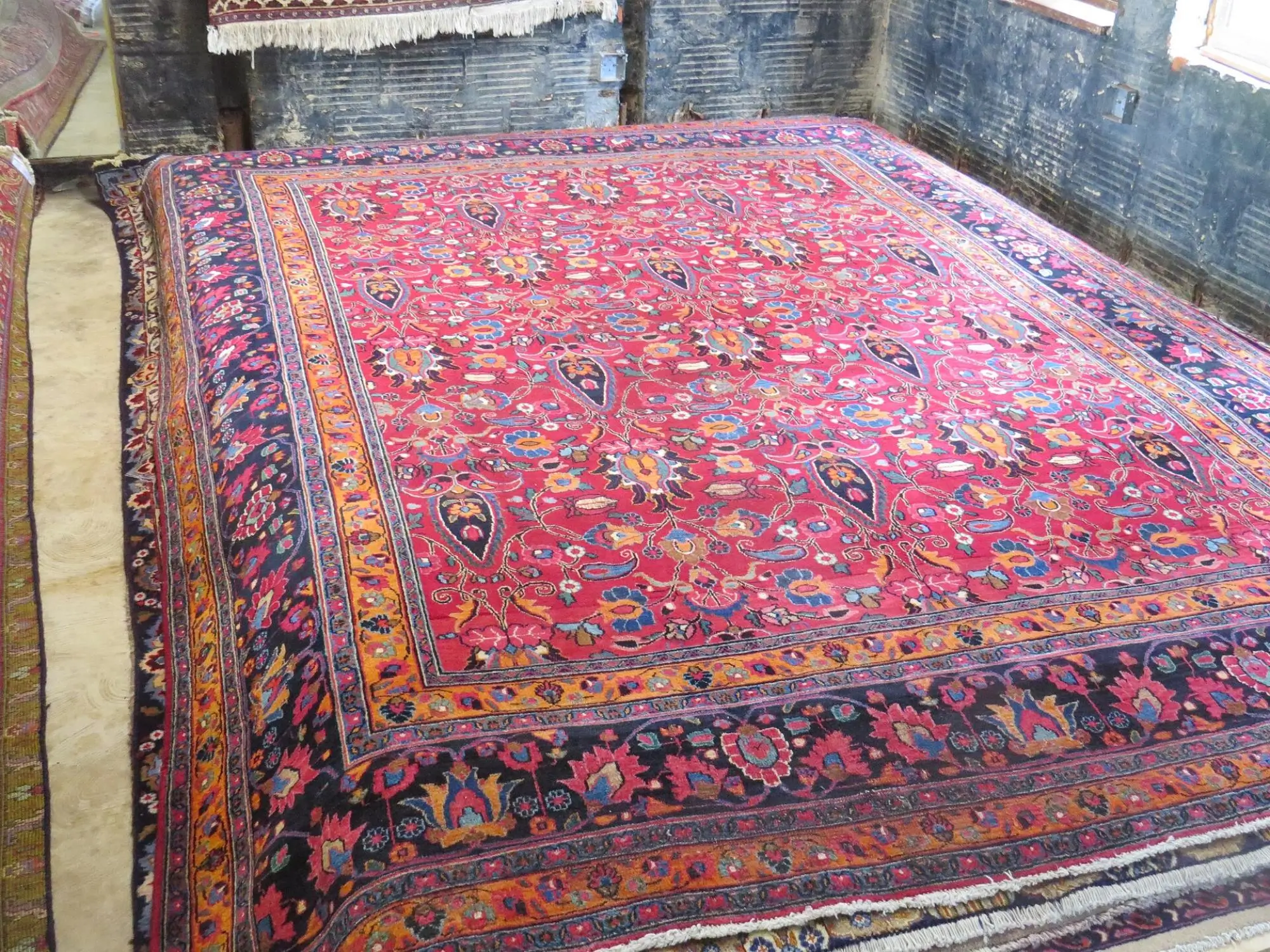 Large colorful Persian-style rug with a red field and ornate floral border laid over a workshop floor.