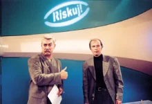 Dva muži stojí ve studiu a nad nimi se skví neonový nápis