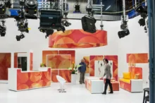 Studio laděné do oranžové a bílé barvy, ve kterém stojí muž a žena