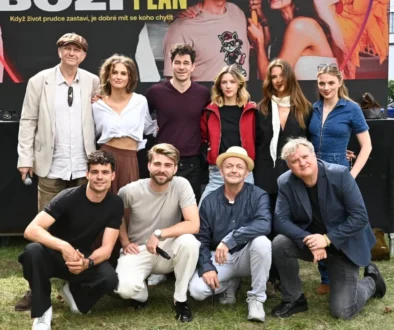 Skupina dospělých lidí různého věku před plakátem s upoutávkou seriálu Boží plán