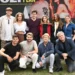 Skupina dospělých lidí různého věku před plakátem s upoutávkou seriálu Boží plán