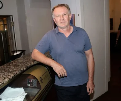 Muž v šedém tričku s límečkem stojí rukou opřený o pult a dívá se před sebe