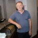 Muž v šedém tričku s límečkem stojí rukou opřený o pult a dívá se před sebe