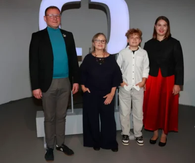 Před velkým logem veřejnoprávní televize stojí jeden dospělý muž, dvě dospělé ženy a jeden malý chlapec