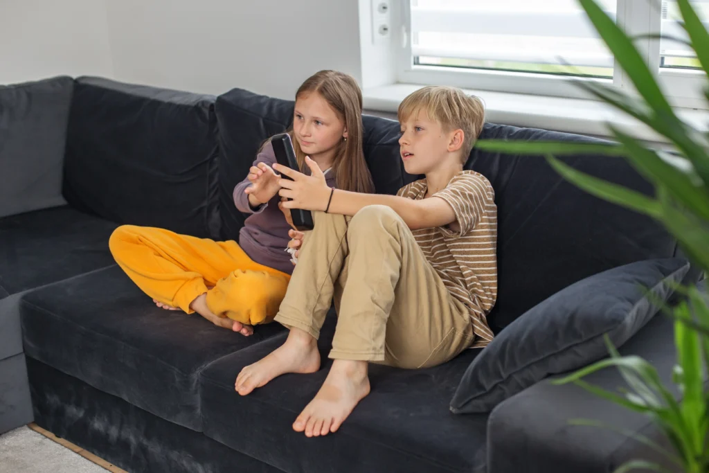 shutterstock_2390616355 - VIPshow Dvě děti sedí v obývacím pokoji na gauči a sledují televizi