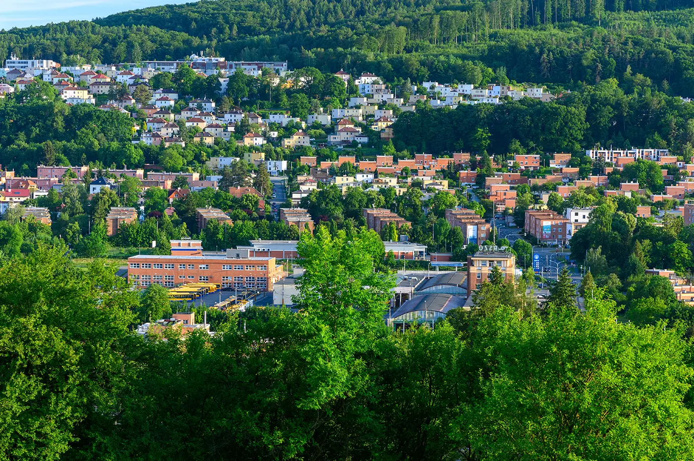 Panoramatický pohled na město Zlín s mnoha domy a zelenými stromy během slunečného dne