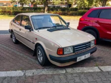Na ulici stojí staré auto ve světlé barvě z osmdesátých let