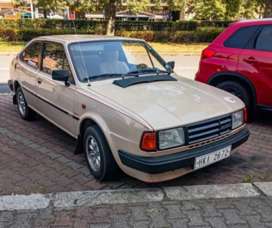 Na ulici stojí staré auto ve světlé barvě z osmdesátých let