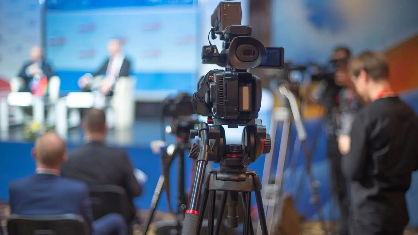 Kamera mířící na nasvícené diskutující lidi ve studiu