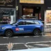 Na ulici stojí modré auto s logem televizní stanice