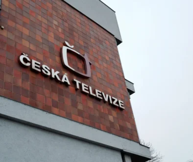Cihlová zeď vysoké budovy a na ní nápis a logo České televize