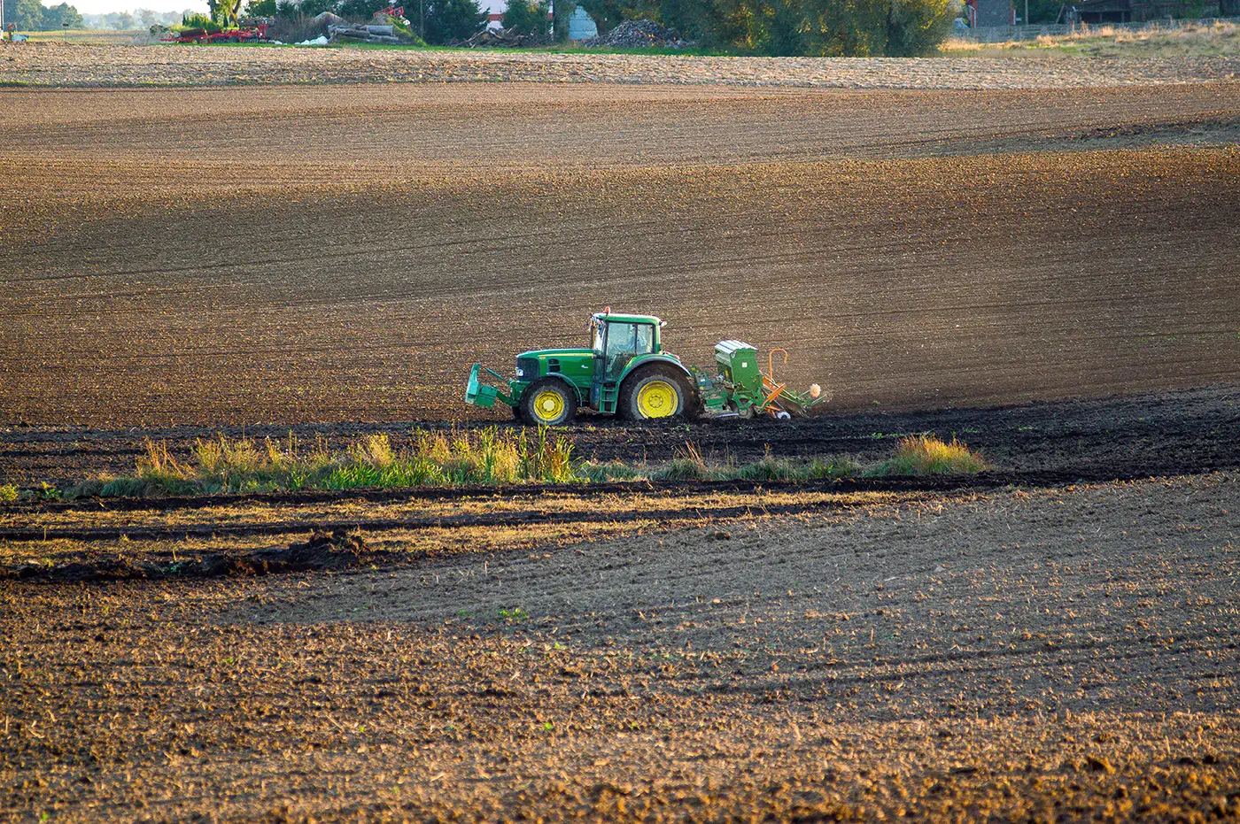 Na poli ve dne jezdí zelený traktor se žlutými koly a orá