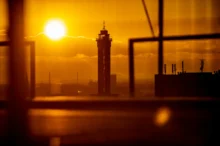 Silhouetted tower against a bright orange sunset with blurred foreground frames in an urban skyline