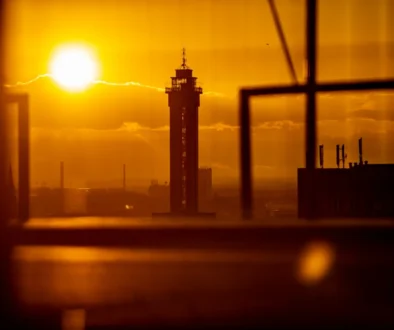 Silhouetted tower against a bright orange sunset with blurred foreground frames in an urban skyline